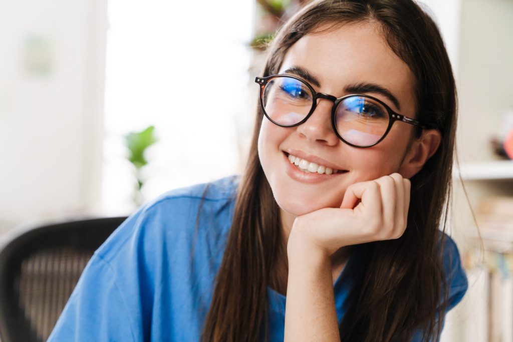 Happy brunette girl in eyeglasses smiling and looking at camera at home